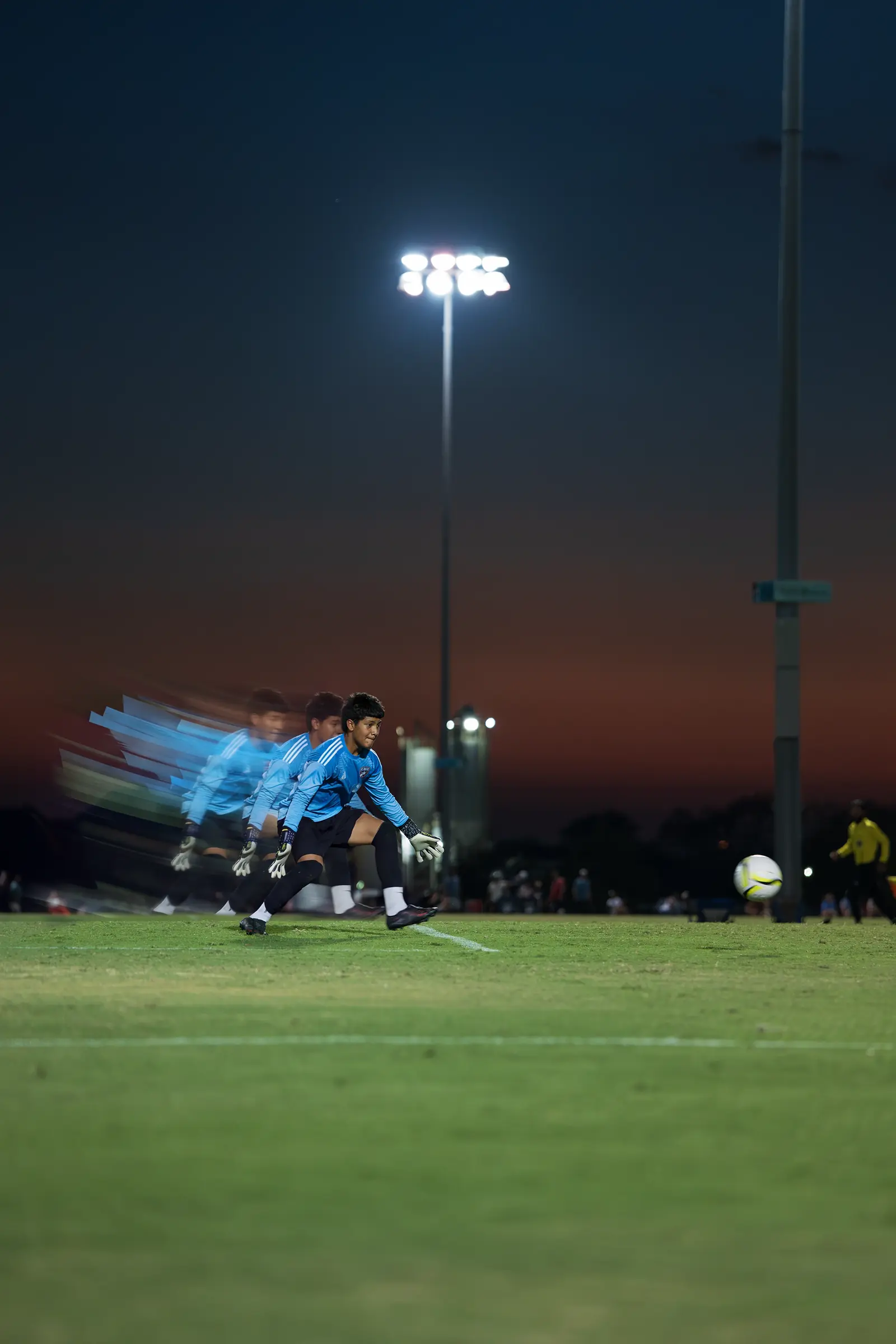 Youth goalkeeper set in a motion-trail edit under stadium lights