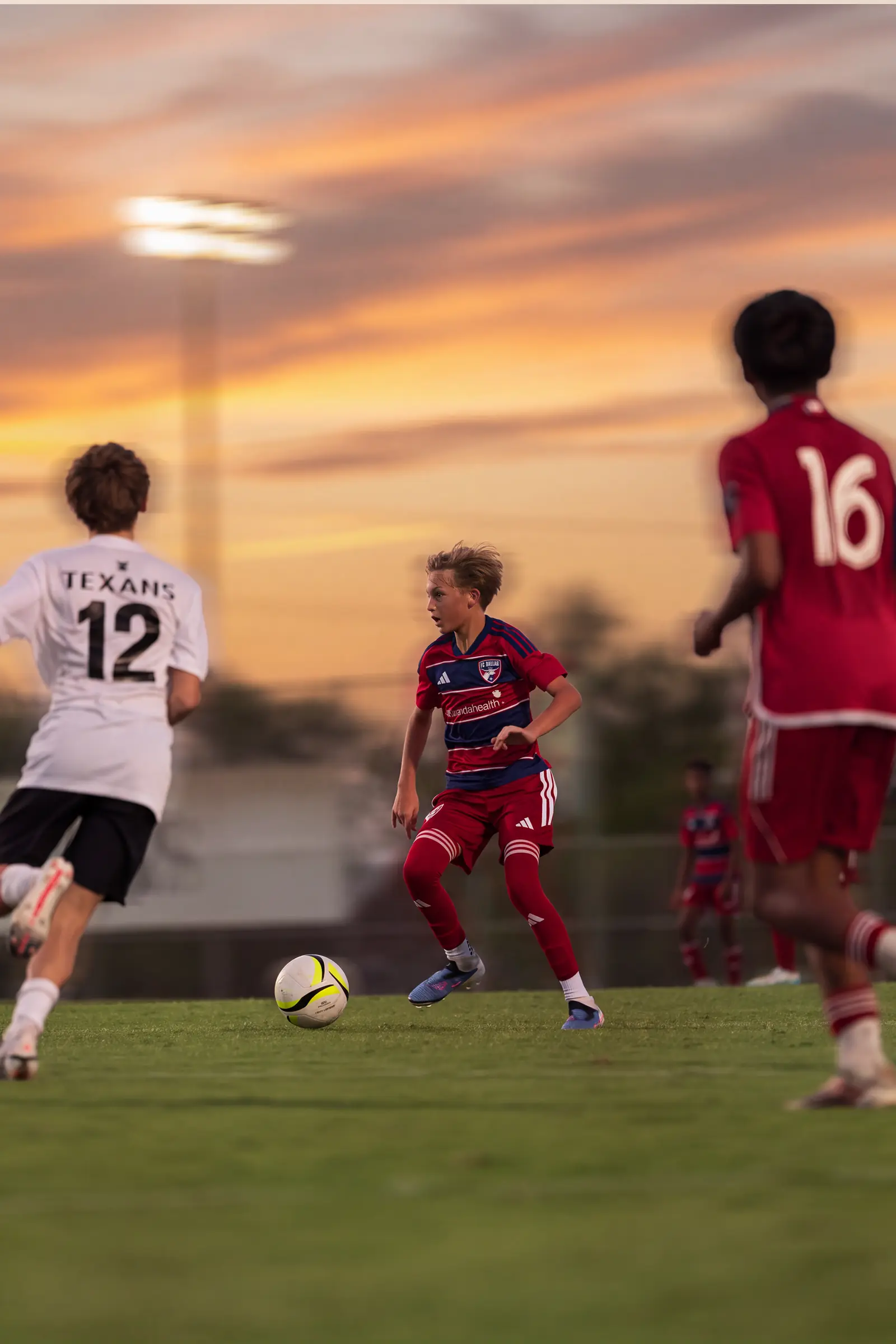 FC Dallas and Texans players chasing the ball under a Dallas sunset