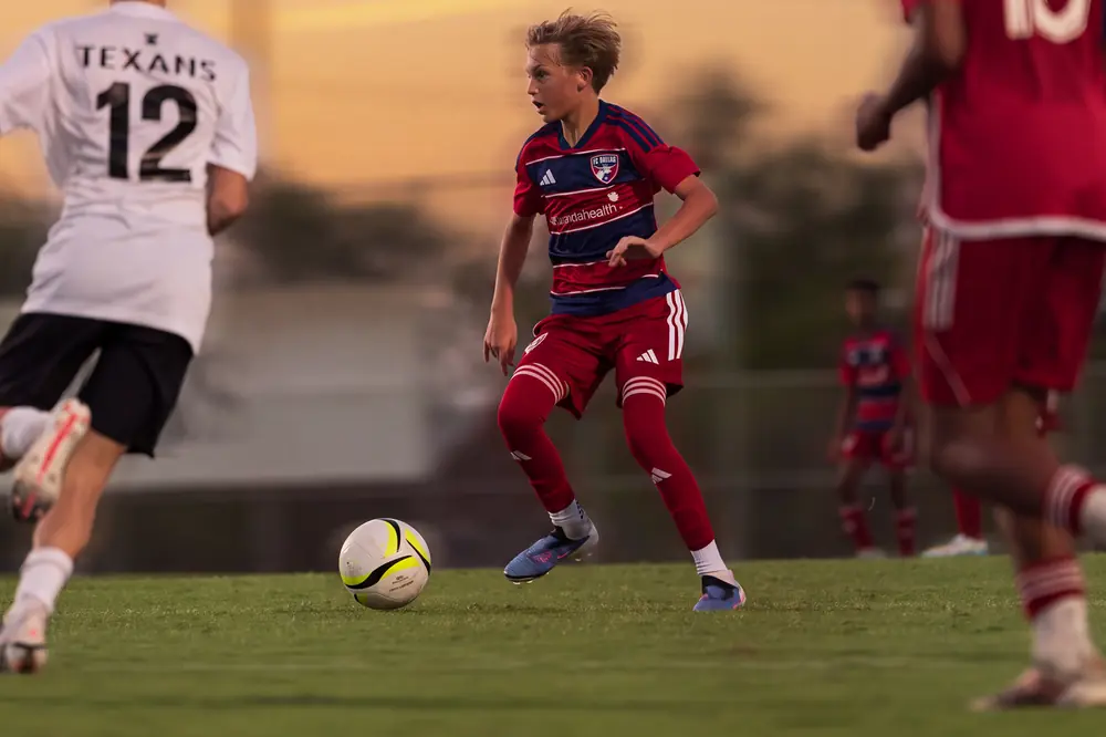 FC Dallas and Texans players chasing the ball under a Dallas sunset