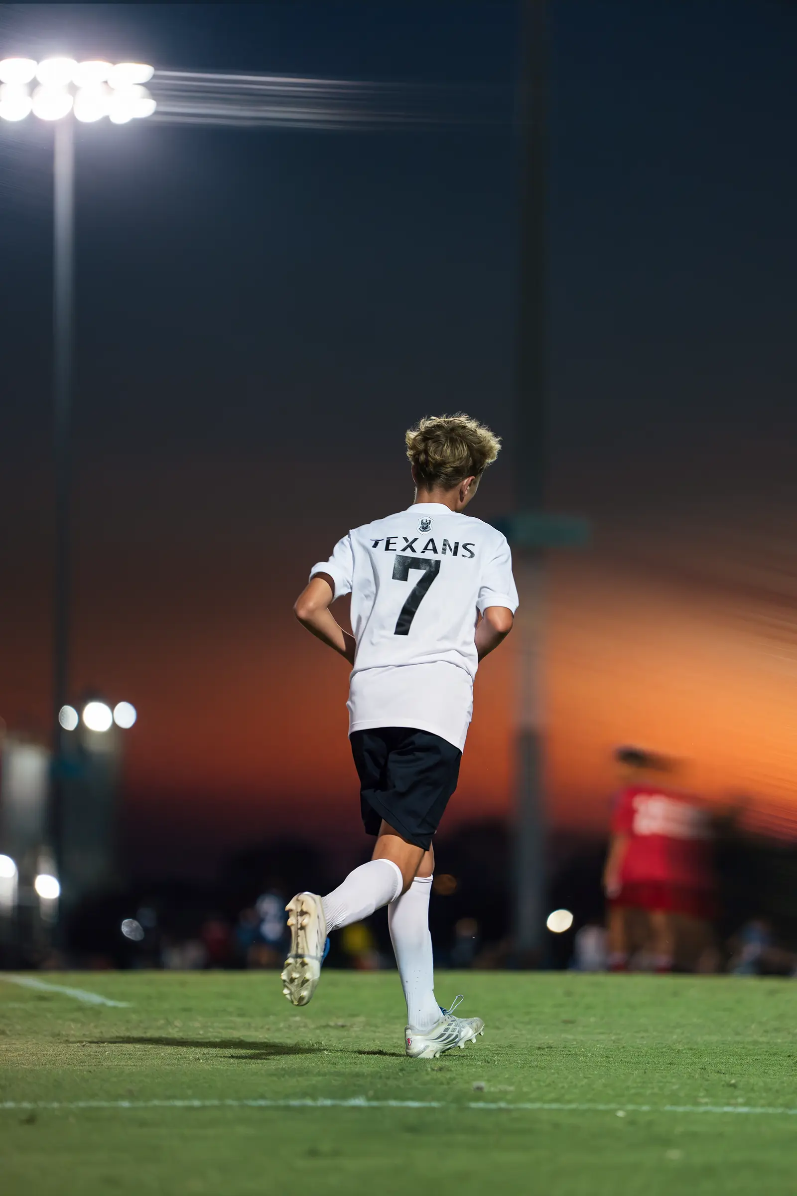 Texans youth player number 7 walking onto the field under stadium lights at dusk in Dallas
